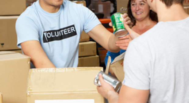 A colour photo of two men and a woman packing boxes for a food donation charity. 