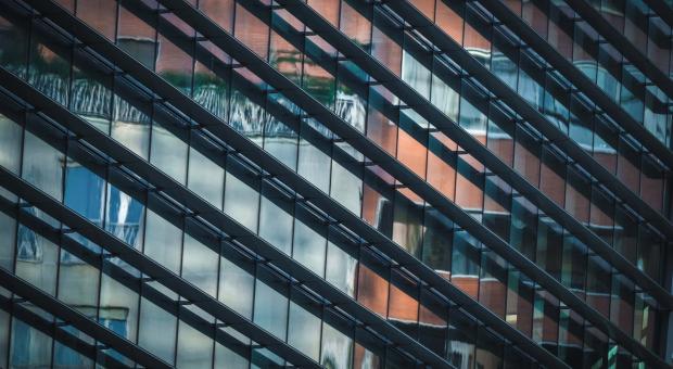 A colour photo of a glass wall skyscraper and reflected in the glass are other high rise buildings.