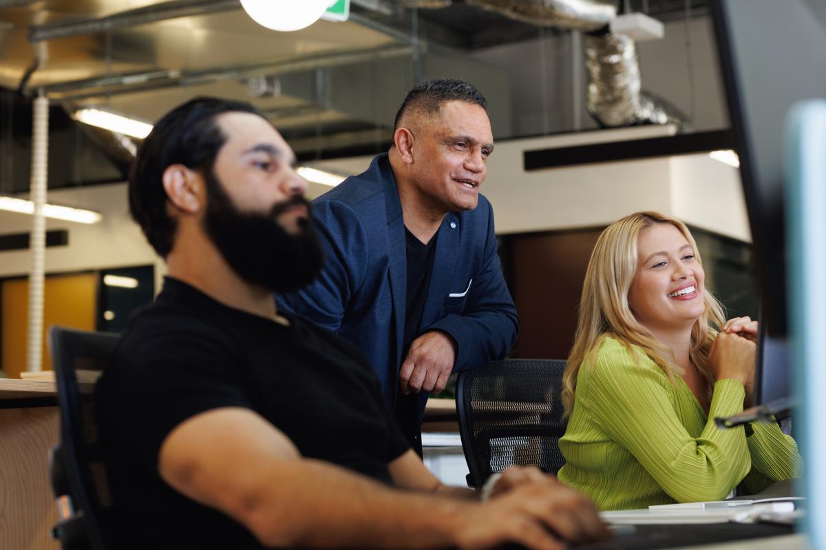 A colour photo of two men and a woman looking at a computer screen. They are smiling and are in an office. 