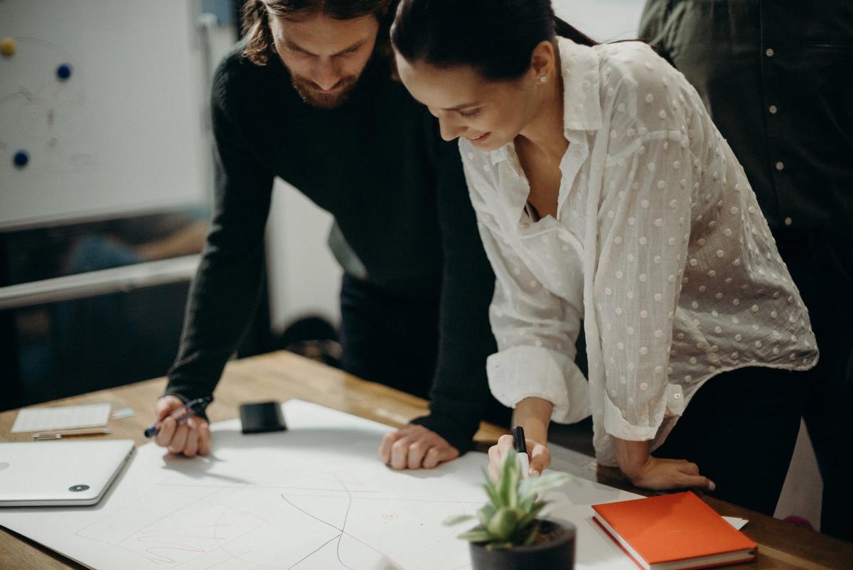 A colour photo of two workers, a man and a woman, in an office looking at plans on an desk in a modern office.