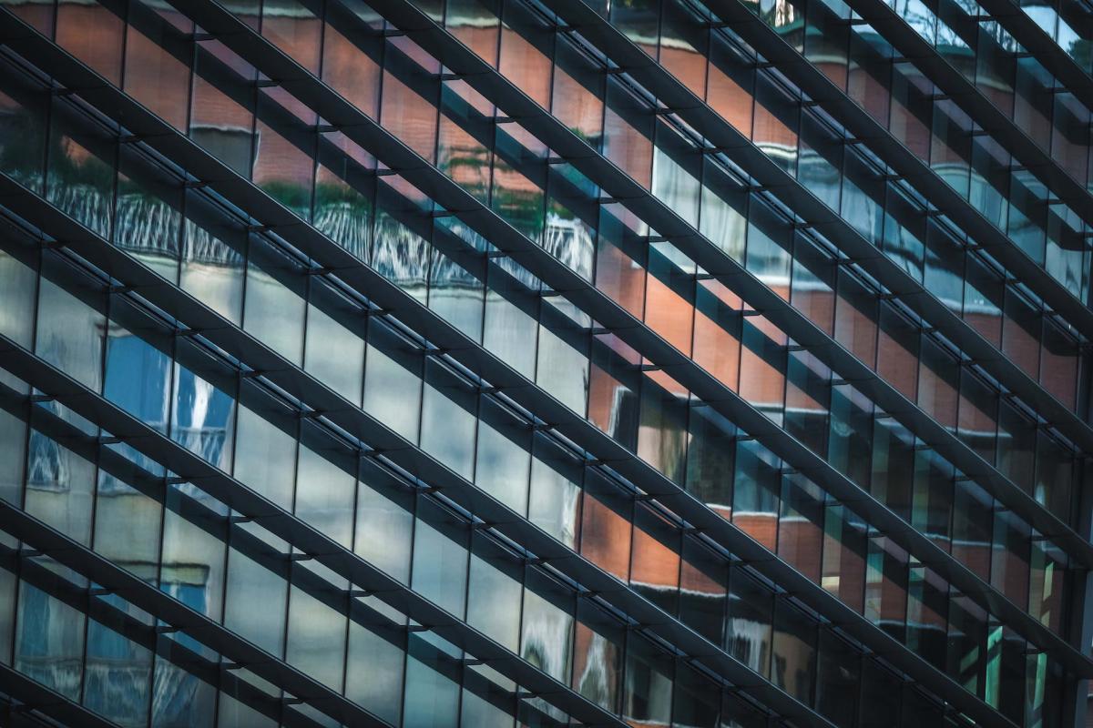 A colour photo of a glass wall skyscraper and reflected in the glass are other high rise buildings.