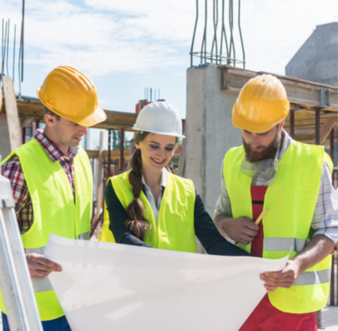 A colour photo of two men and a woman in bright yellow construction attire looking at a building plan in a construction zone.