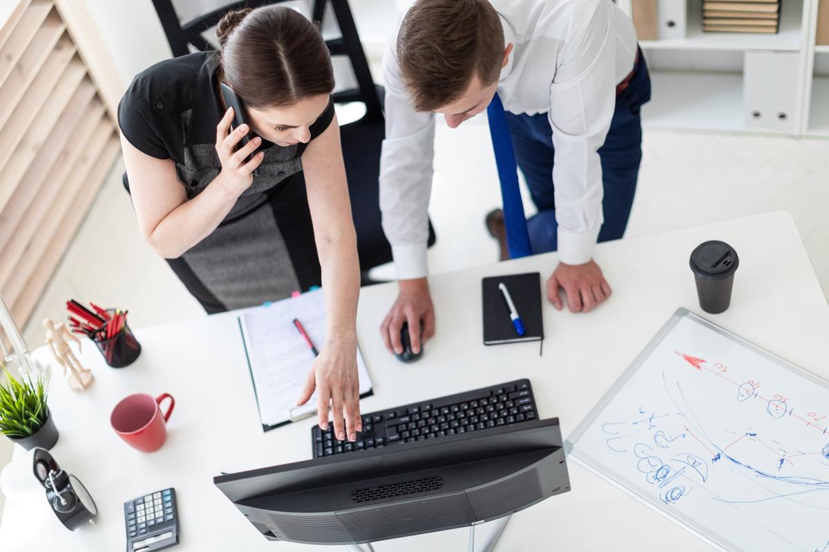 A colour photograph of young people in the office, looking at a laptop. 