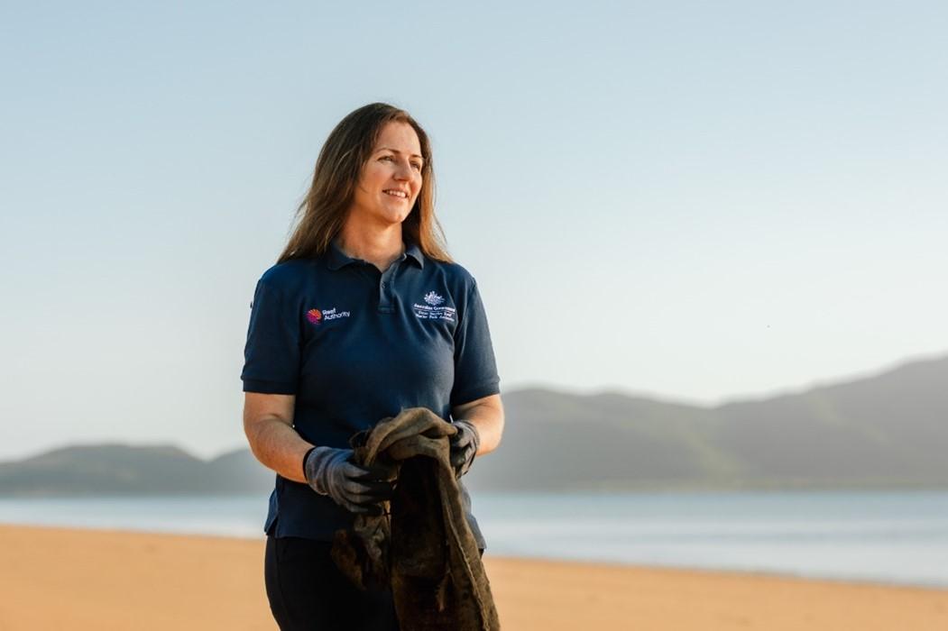 A photo of a woman walking along the beach. She is smiling and looking at the water.